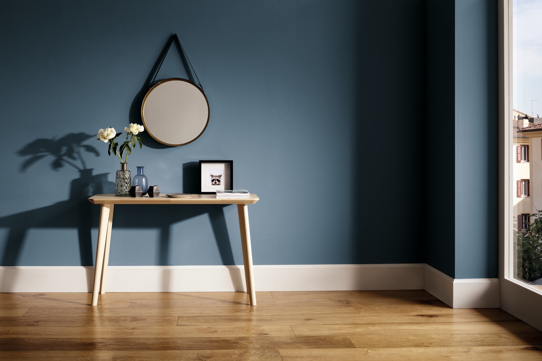 Modern living room with natural wood parquet flooring, high baseboards, and deep blue walls