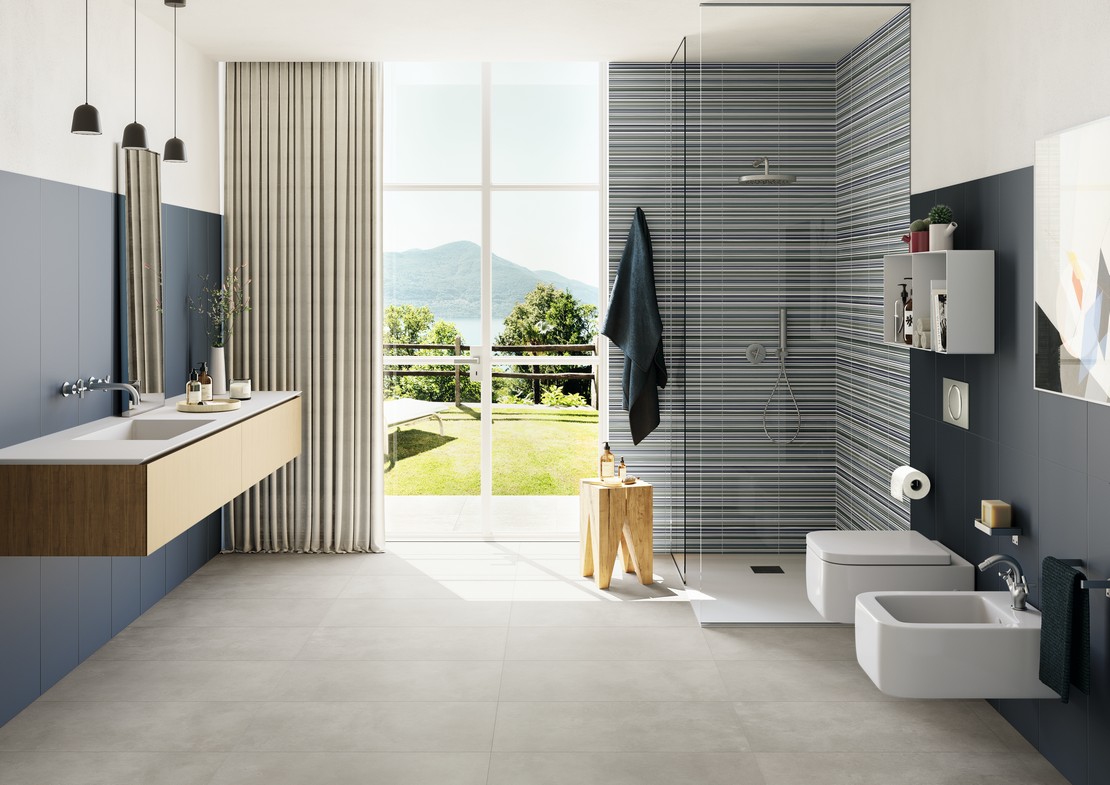 Bagno moderno con pavimento effetto cemento grigio e rivestimento effetto carta da parati blu - Ambienti Iperceramica